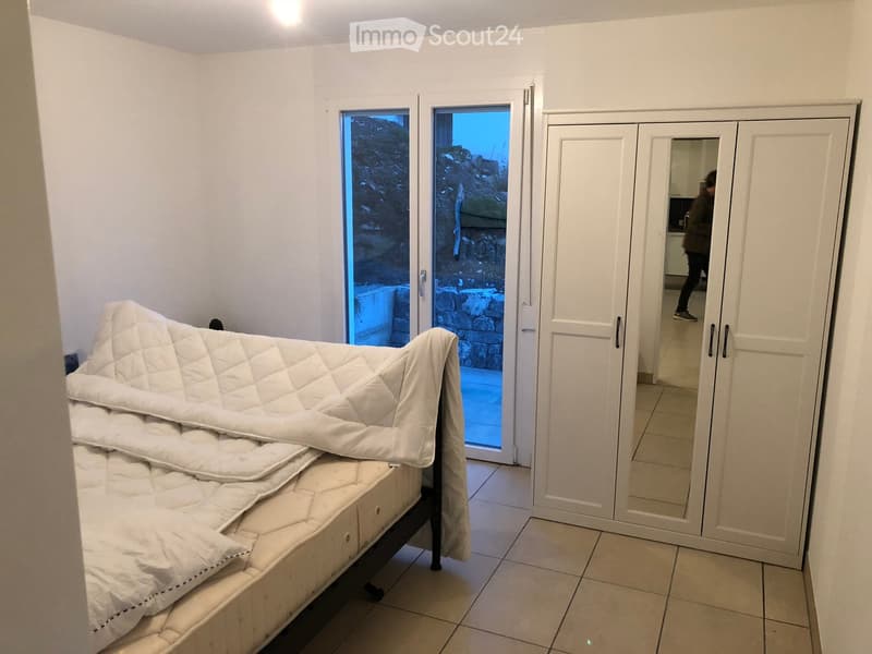 Bedroom with a white bed and quilt, a large mirrored wardrobe, and a sliding glass door leading to an outdoor area.