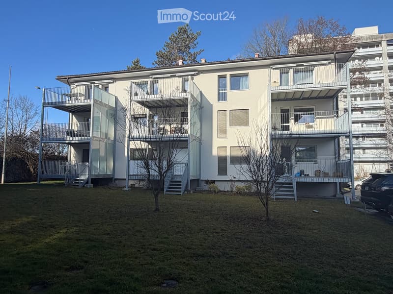 Modern two-story residential building with balconies, glass railings, and a small front lawn.