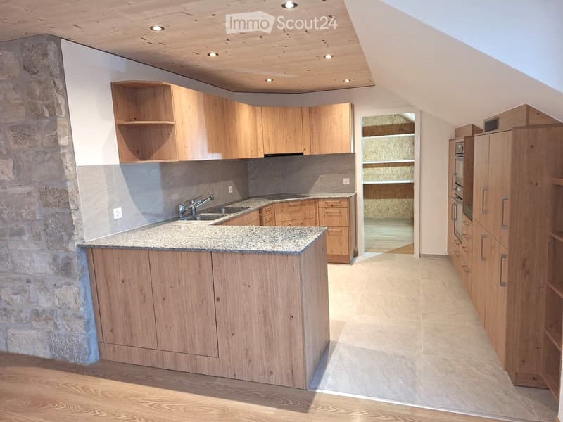 Modern kitchen with wooden cabinets, granite countertop, sink, and faucet. Features a stone wall and recessed lighting.