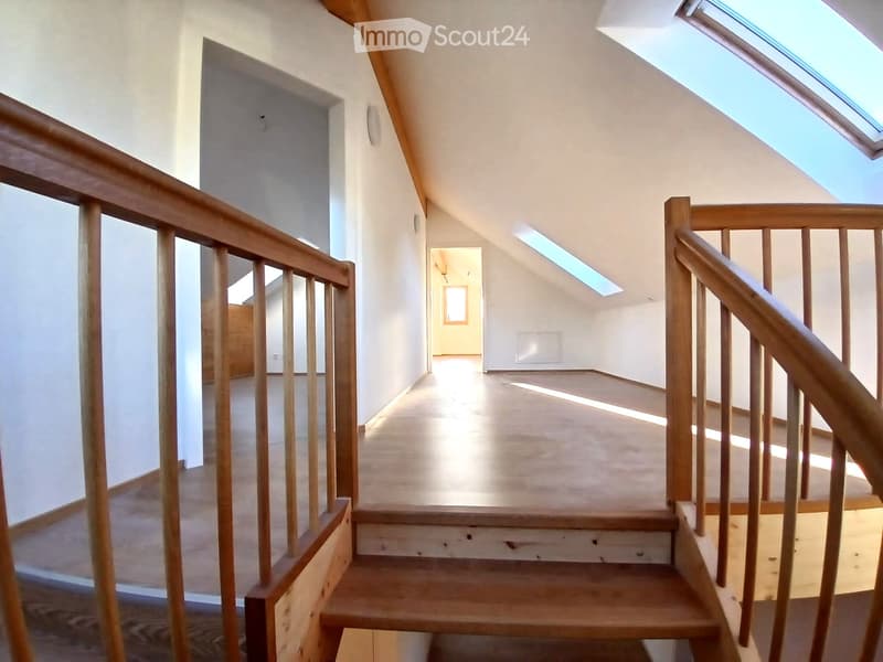 Spacious, well-lit hallway with wooden staircase and railings, leading to an open area with skylights.
