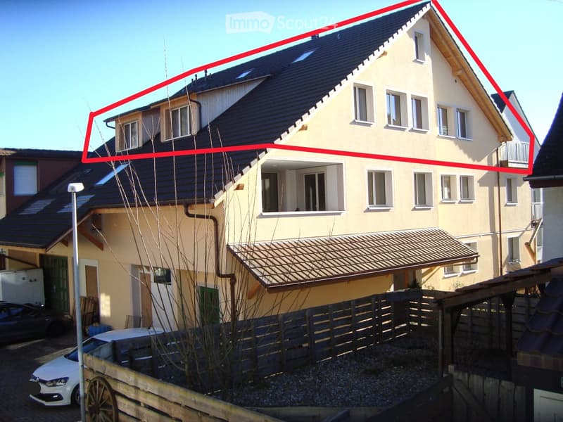 Two-story house with beige exterior, dark roof, multiple windows, and a covered entrance area.