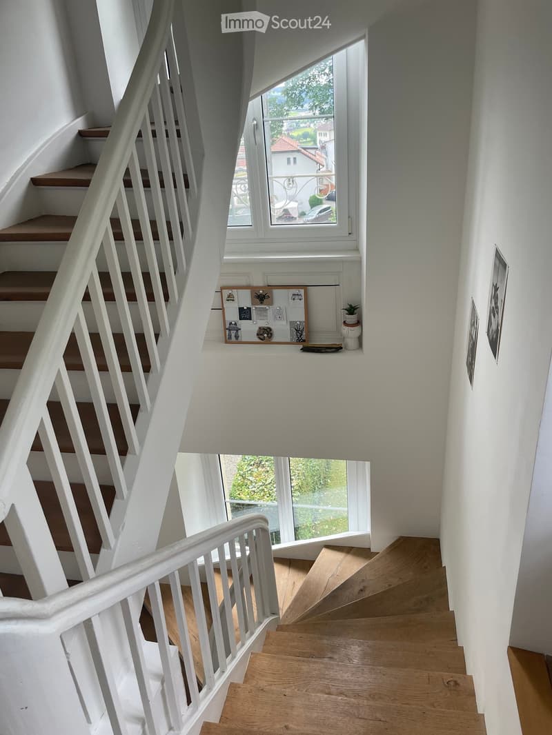 Staircase with wooden steps and white railings, leading to a landing area with a small window and a potted plant on the windowsill.