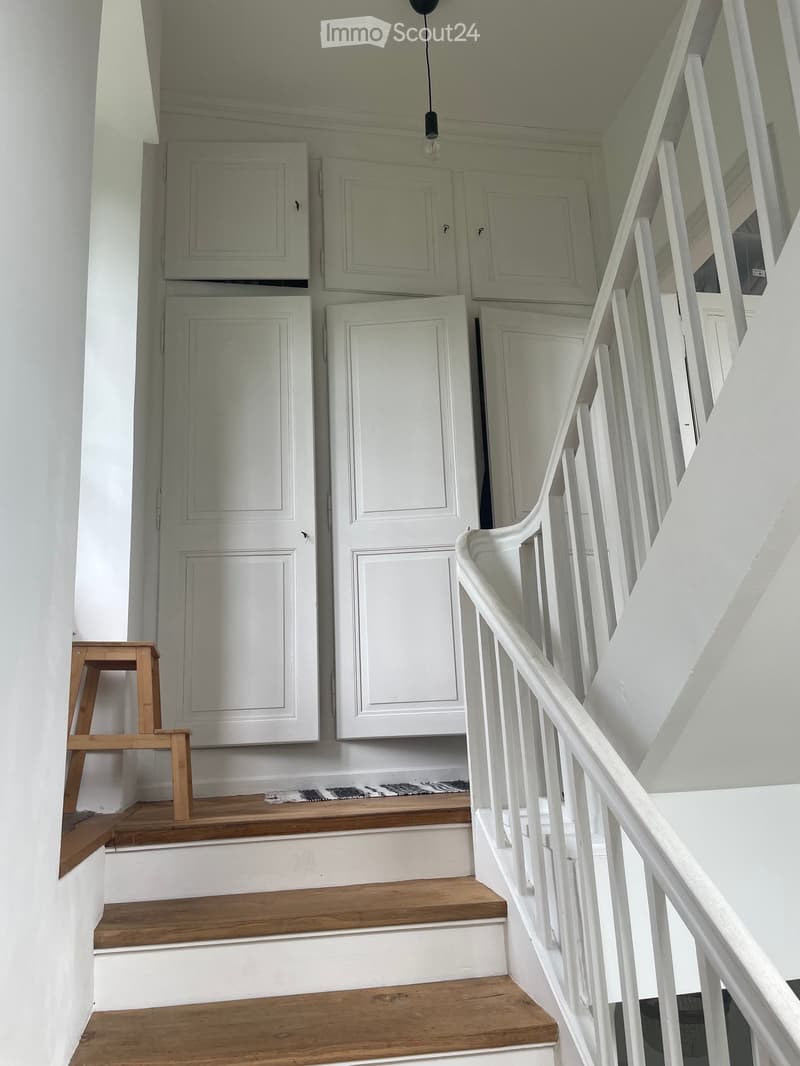 Wooden staircase with white railings and wooden steps, small wooden stool on the landing, white cabinets on the wall.