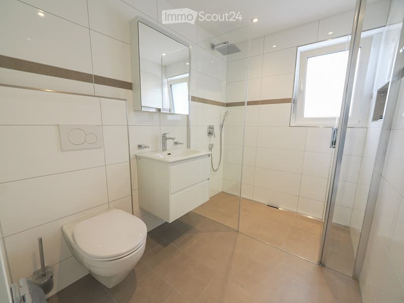 Modern bathroom with white tiles, a toilet, a sink with a mirror, and a glass-enclosed shower area.