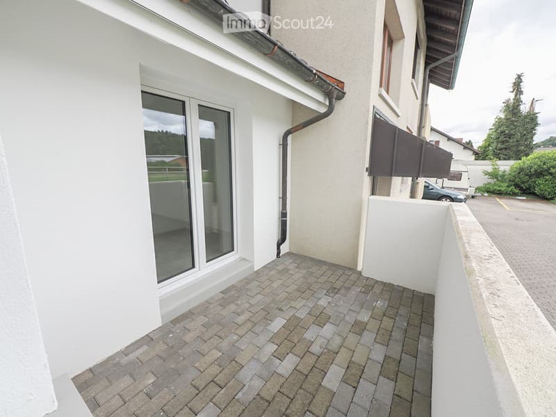 Balcony with brick paving, large window, and white walls.