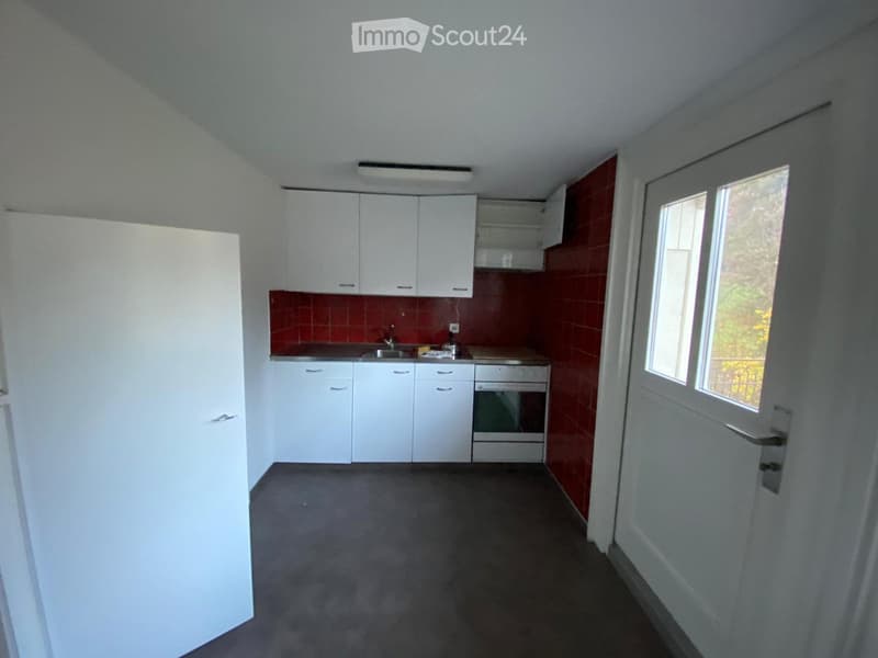 Empty kitchen with white cabinets, red tiled backsplash, and a window on the right side.