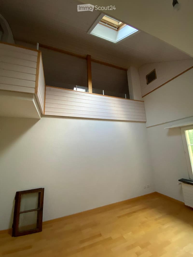 Empty room with wooden flooring, white walls, and a skylight window. There is a small balcony area visible through an open doorway.
