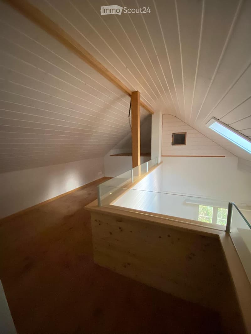Modern, open staircase with wooden railings and glass balustrades, leading to an attic space with exposed wooden beams and skylight windows.