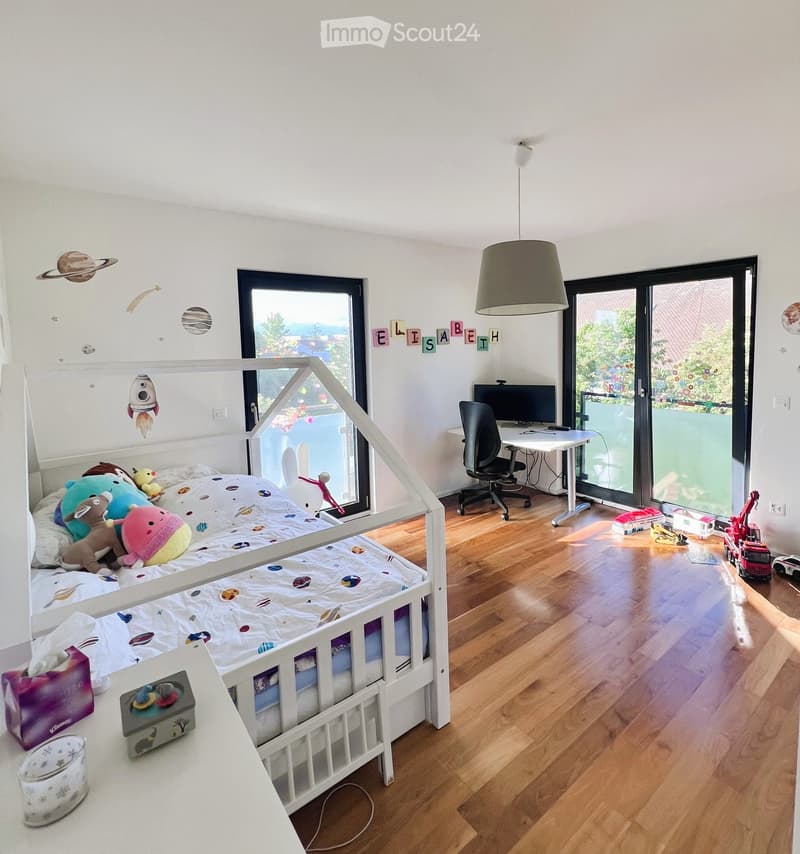 A well-lit children's bedroom with a bunk bed, desk, and various toys. The room features a large window with a view, a hanging lamp, and decorative wall elements.