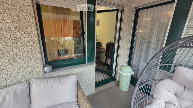 Balcony with two wicker chairs, cushions, a small trash can, and an open door leading to an interior space.