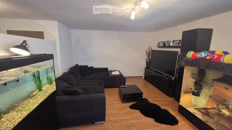 Modern living room with a dark sectional sofa, coffee table, fish tank, TV, and decorative items on shelves.