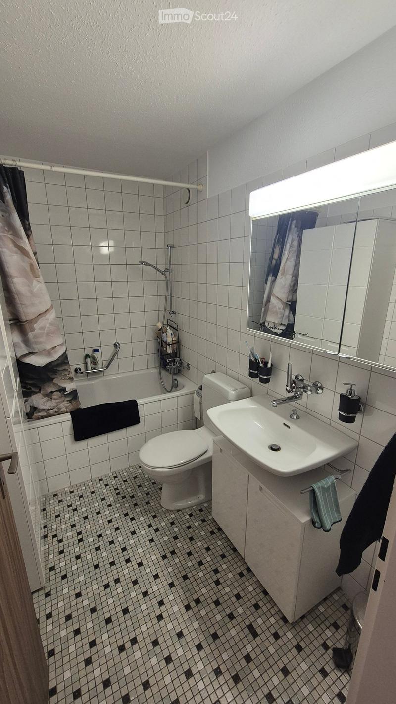 A compact bathroom with white tiled walls, a black and white checkered floor, a toilet, a sink with a mirror, a bathtub, and various toiletries.