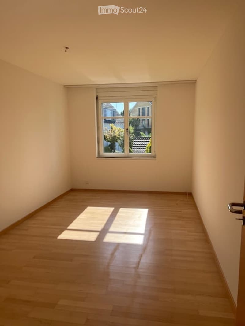 Empty room with wooden flooring and a single window allowing natural light to enter.