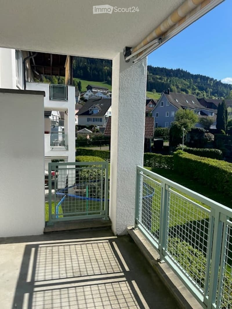 Balcony with metal railing, retractable awning, and scenic view of a residential area with houses and greenery.