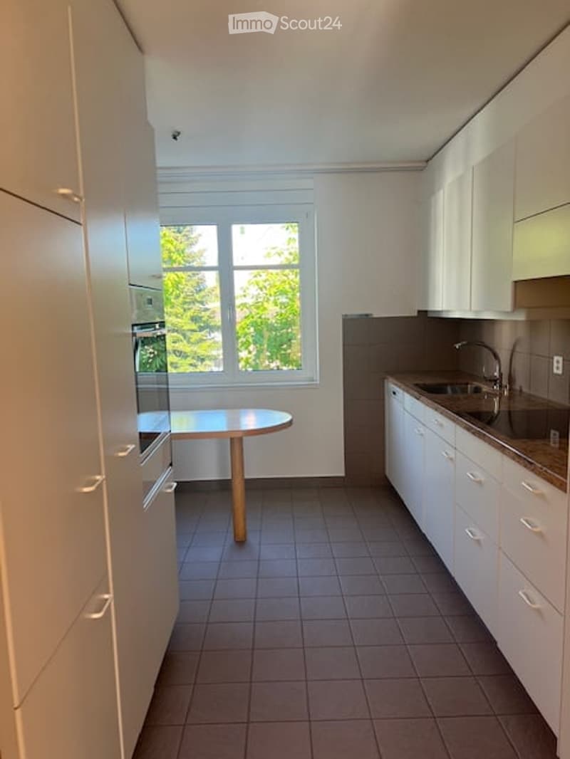 Modern kitchen with white cabinets, dark tiled floor, and a small round wooden table near the window.