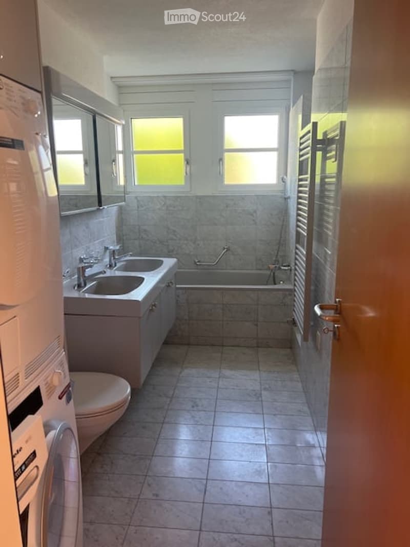 Modern bathroom with double sink, large mirror, bathtub, and tiled floor.