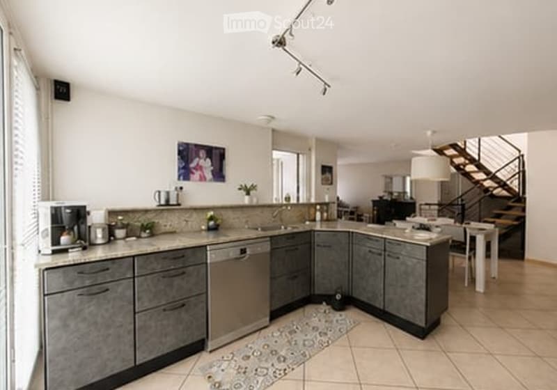 Modern kitchen with grey cabinets, stainless steel appliances, a coffee maker, sink, and a small dining area with a table and chairs.