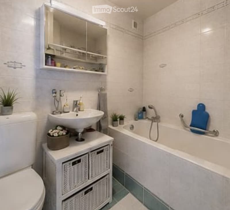 Modern bathroom with white tiles, a bathtub, a toilet, a sink, a mirror cabinet, a shower chair, and a small storage unit with wicker baskets.