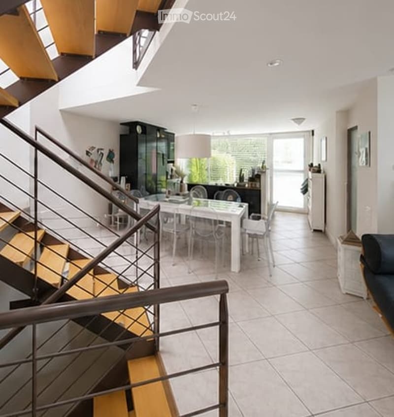 Open-plan living and dining area with modern furniture, including a white dining table with chairs, a dark blue sofa, and a staircase leading to an upper level.