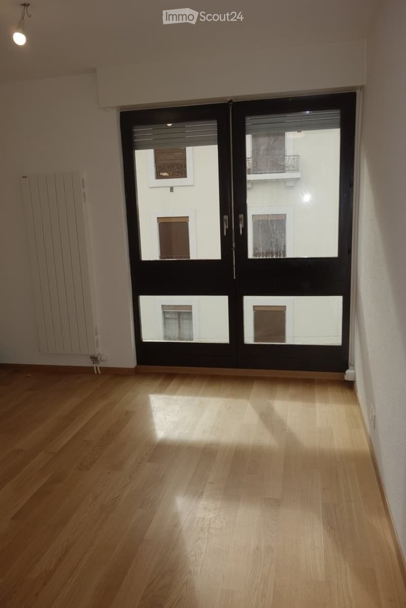 Empty room with wooden flooring, large sliding glass doors, and a radiator on the wall.