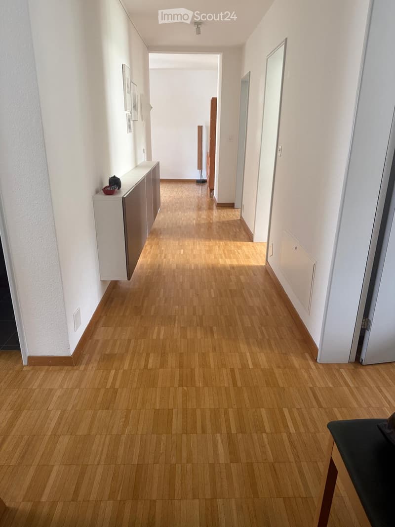 Clean, well-lit hallway with wooden flooring, white walls, and several doors leading to other rooms.