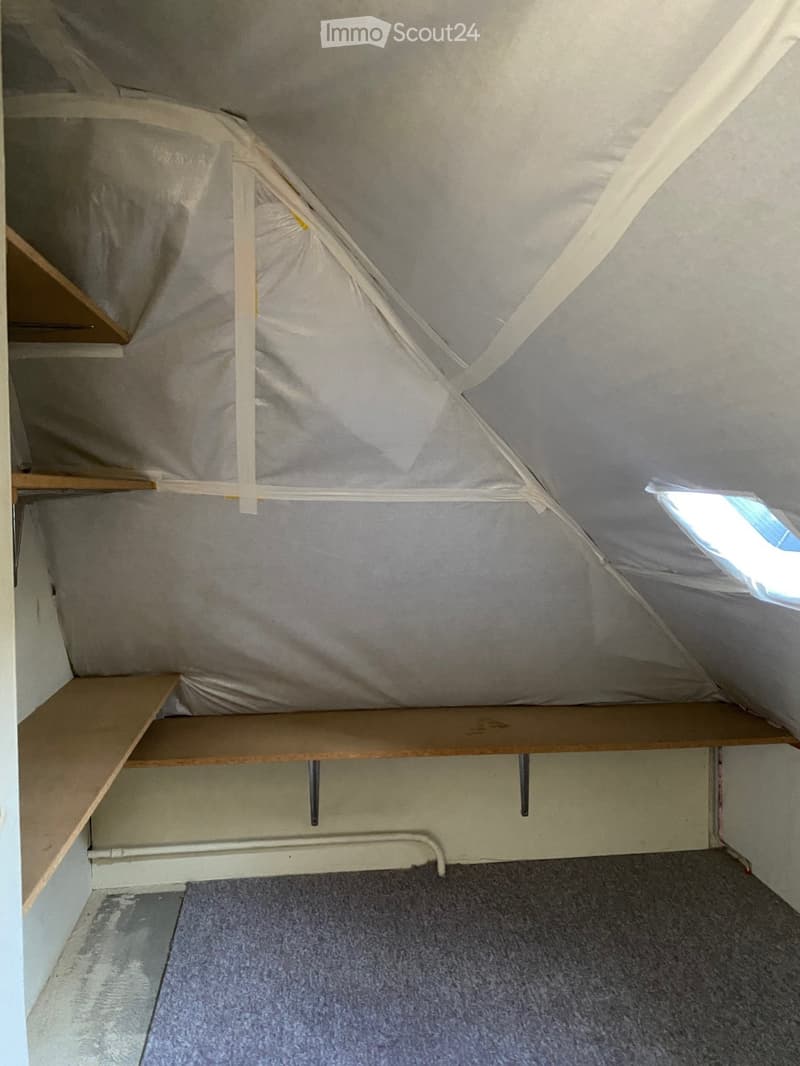 Empty room, slanted ceiling, wooden shelves, metal bracket support, white insulation, window, carpeted floor.