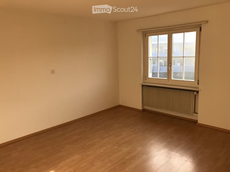 Empty room with wooden flooring, light-colored walls, and a window with a radiator below it.