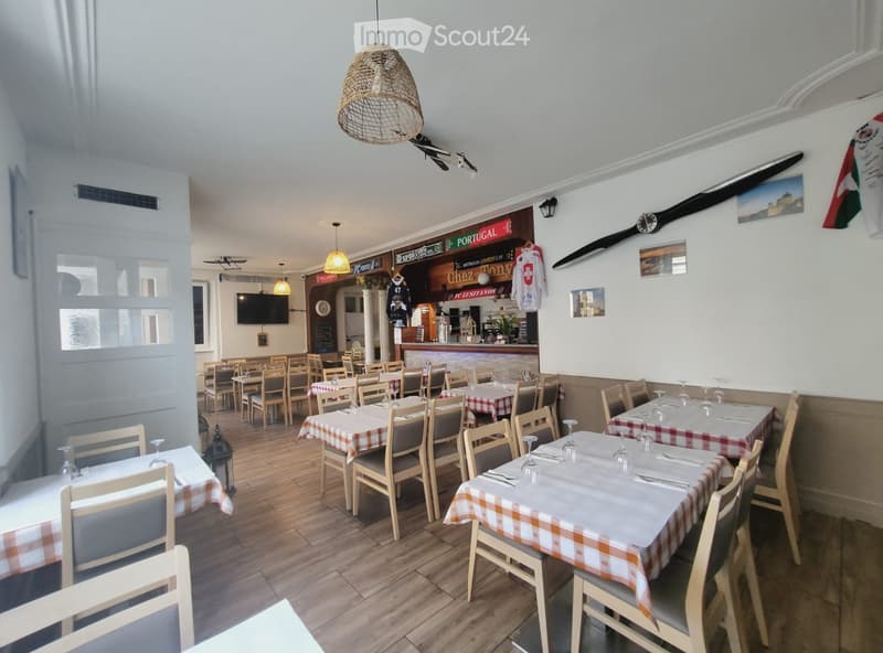 Restaurant interior with wooden tables and chairs, checkered tablecloths, wine glasses, and a television in the background.