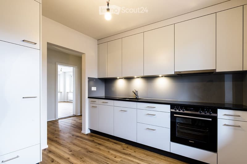 Modern kitchen with white cabinets, black countertops, and stainless steel appliances, including an oven and a sink with a faucet.