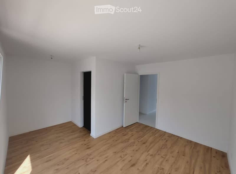 Empty room with white walls, wooden flooring, and two doors, one leading to another room.