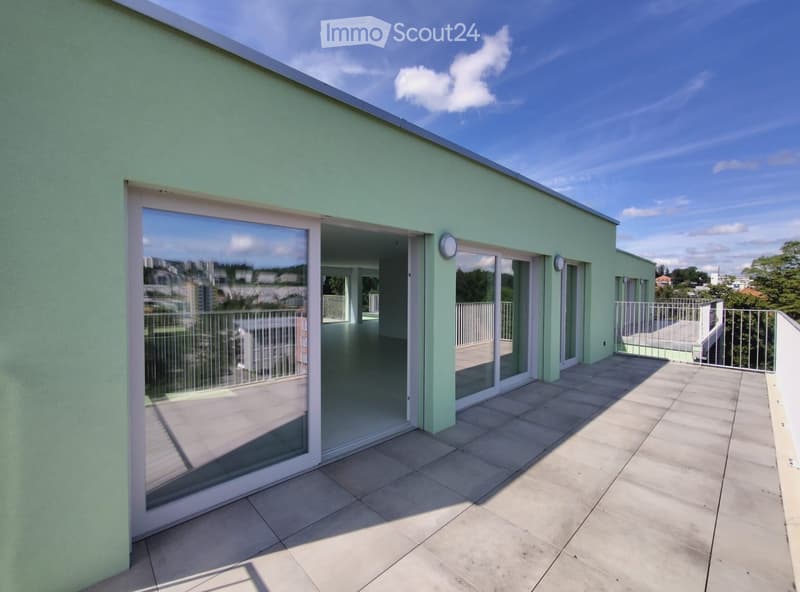 A modern balcony with tiled flooring, glass sliding doors, and metal railings, offering a view of the cityscape.