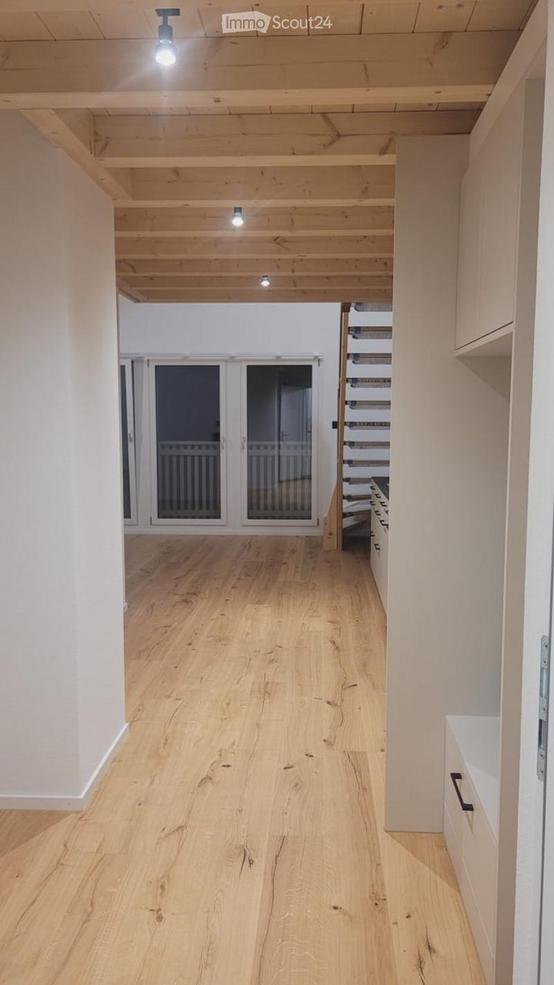 Bright, open hallway with light wooden flooring and white walls, leading to a staircase and large glass doors.
