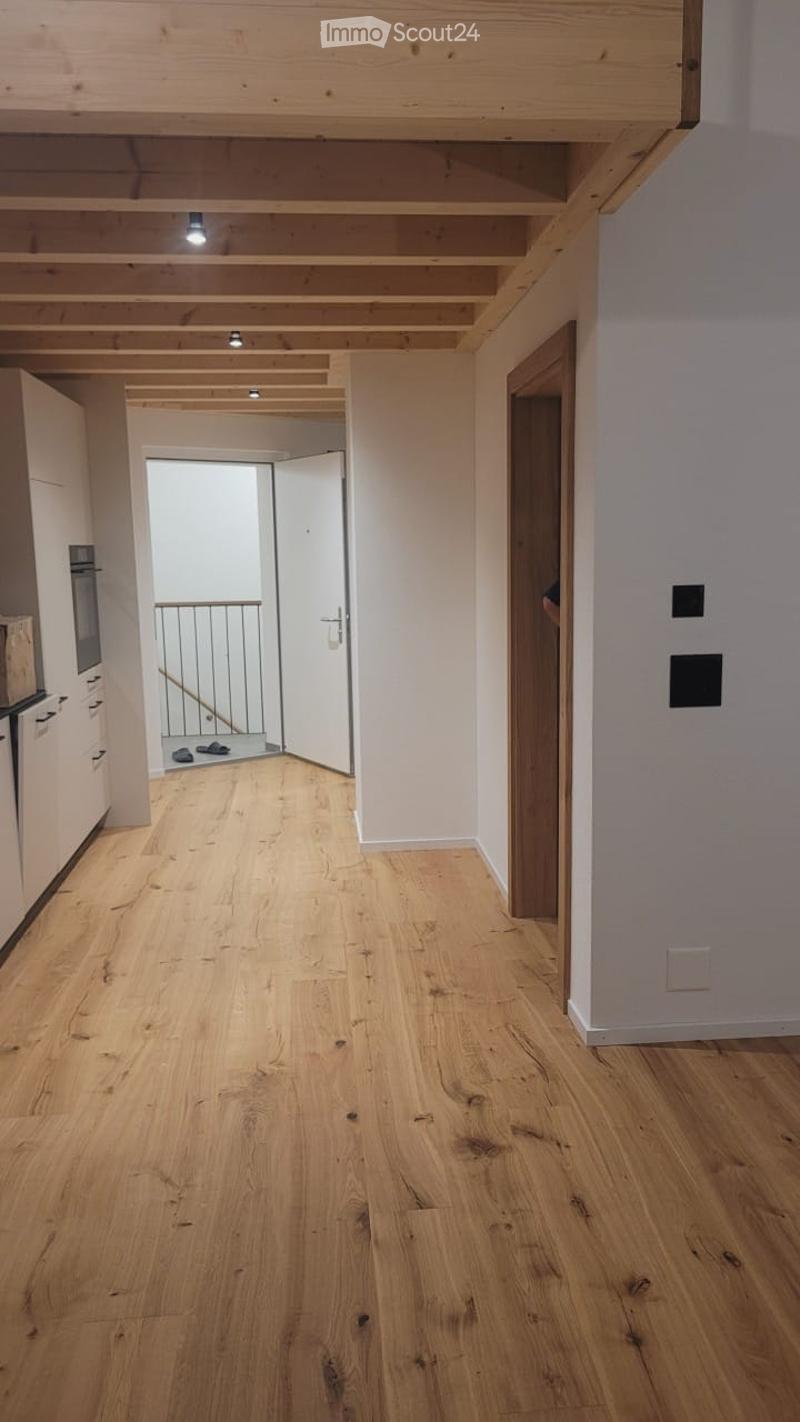 Bright, open hallway with light wooden flooring and white walls. Features exposed wooden beams on the ceiling, recessed lighting, and a staircase leading to an upper level.