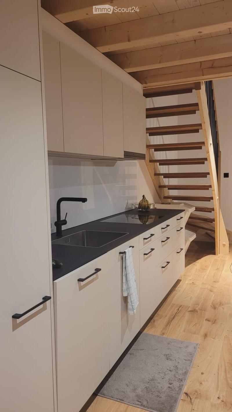 Modern kitchen with white cabinets, black countertop, sink, faucet, and a small staircase leading upwards.