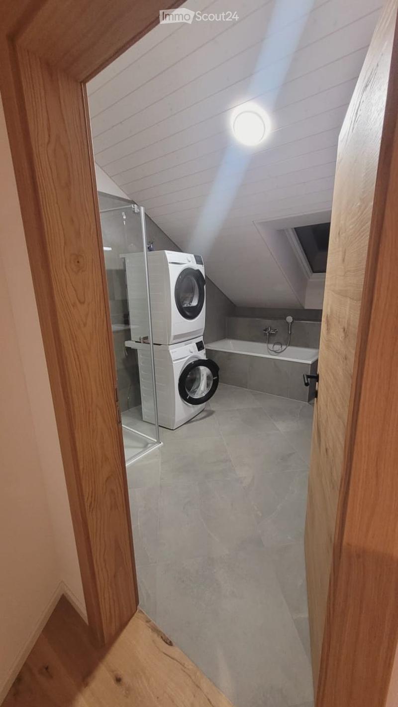 Attic bathroom with a washing machine, bathtub, and skylight window providing natural light.