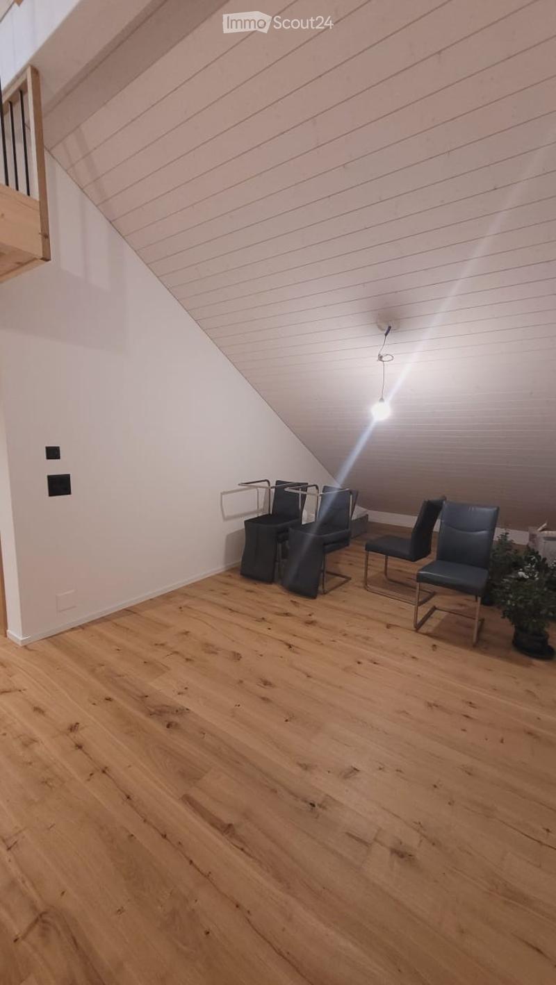 Attic room with wooden flooring, slanted white ceiling, and modern chairs and a small table near the wall.