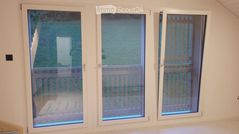Empty room with three large white-framed sliding doors leading to a balcony or outdoor area, featuring glass panels and metal railings.