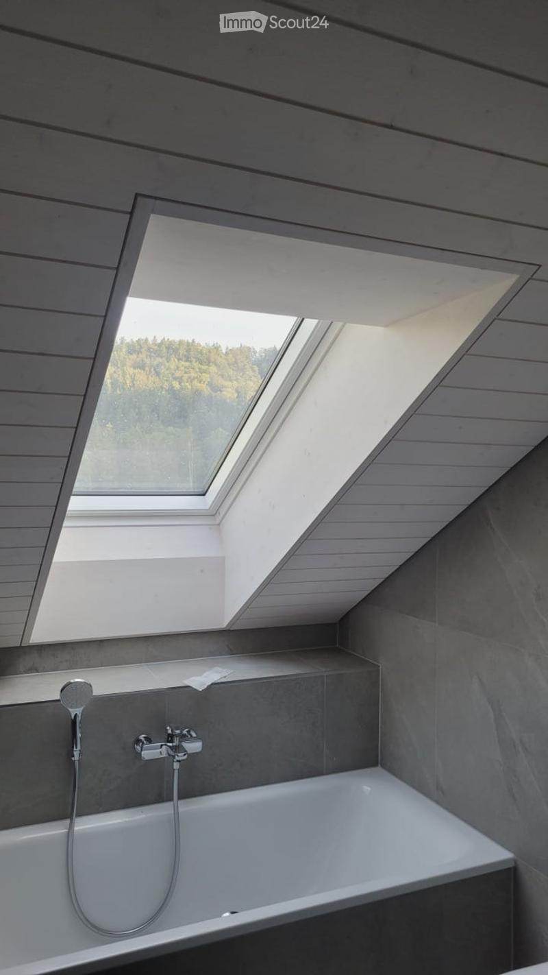 Modern bathroom with a bathtub, sleek faucet, and skylight windows offering a view of the forest.