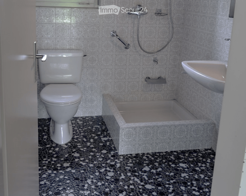 Bathroom with white tiled walls, a toilet, a bathtub, a sink, and a shower hose.