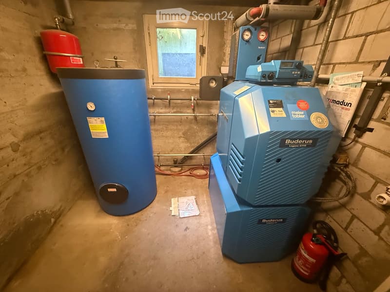 Utility room with a water heater, boiler, and fire extinguisher, featuring a small window and concrete walls.