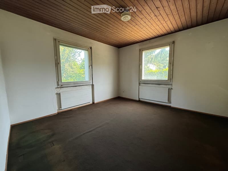 Empty room with wooden ceiling, carpeted floor, white walls, two windows, and radiators.