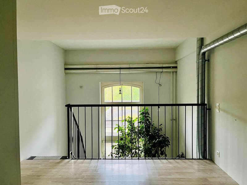 Balcony with wooden floor, metal railing, and a window overlooking greenery.