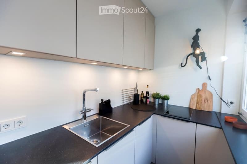 Modern kitchen with white cabinets, black countertops, stainless steel sink, and various small appliances and decor items.