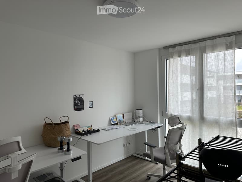 Modern, minimalist office space with a white desk, ergonomic chair, laptop, and decorative items including a woven basket and picture frames.