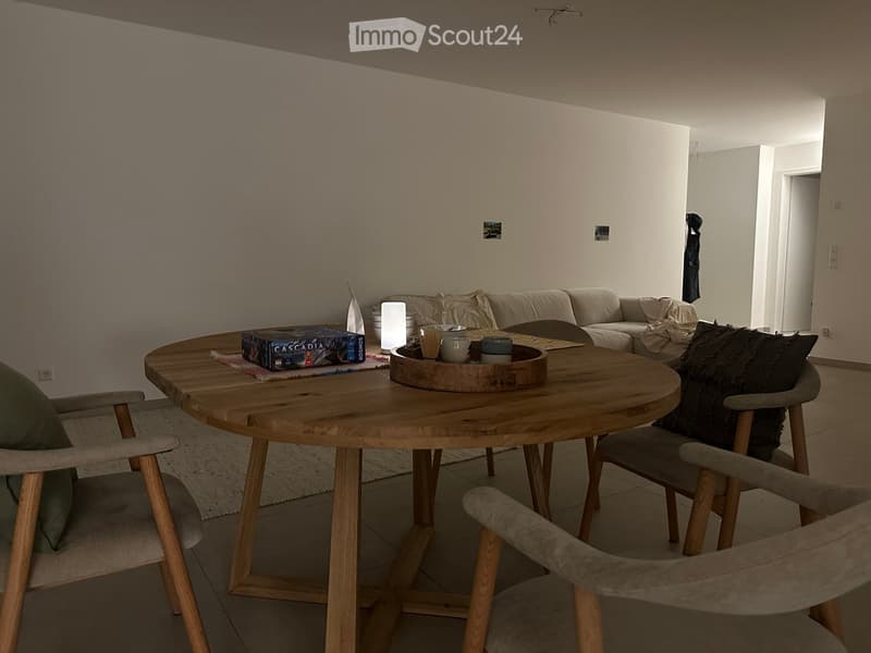 Modern living room with a round wooden coffee table, sofa, chairs, and decorative items including a board game and a tray with cups.