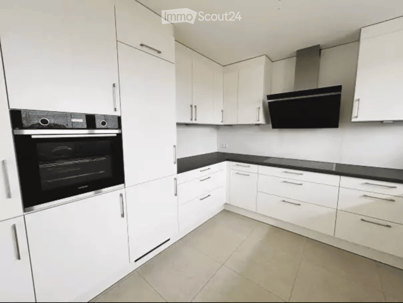 Modern kitchen with white cabinets, black countertops, and stainless steel appliances including an oven and range hood.