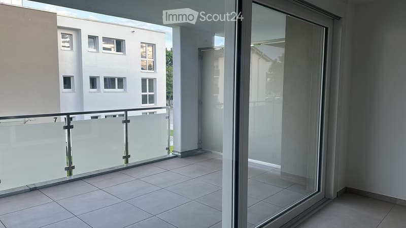 Modern balcony with tiled floor, glass railing, and sliding glass door leading to the interior.