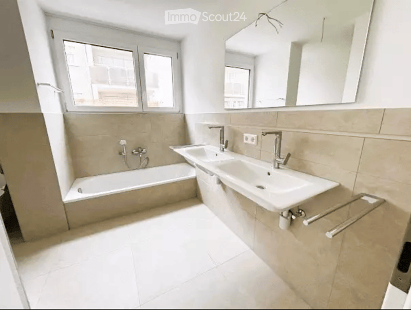 Modern bathroom with a bathtub, double sink, large mirror, and tiled walls.