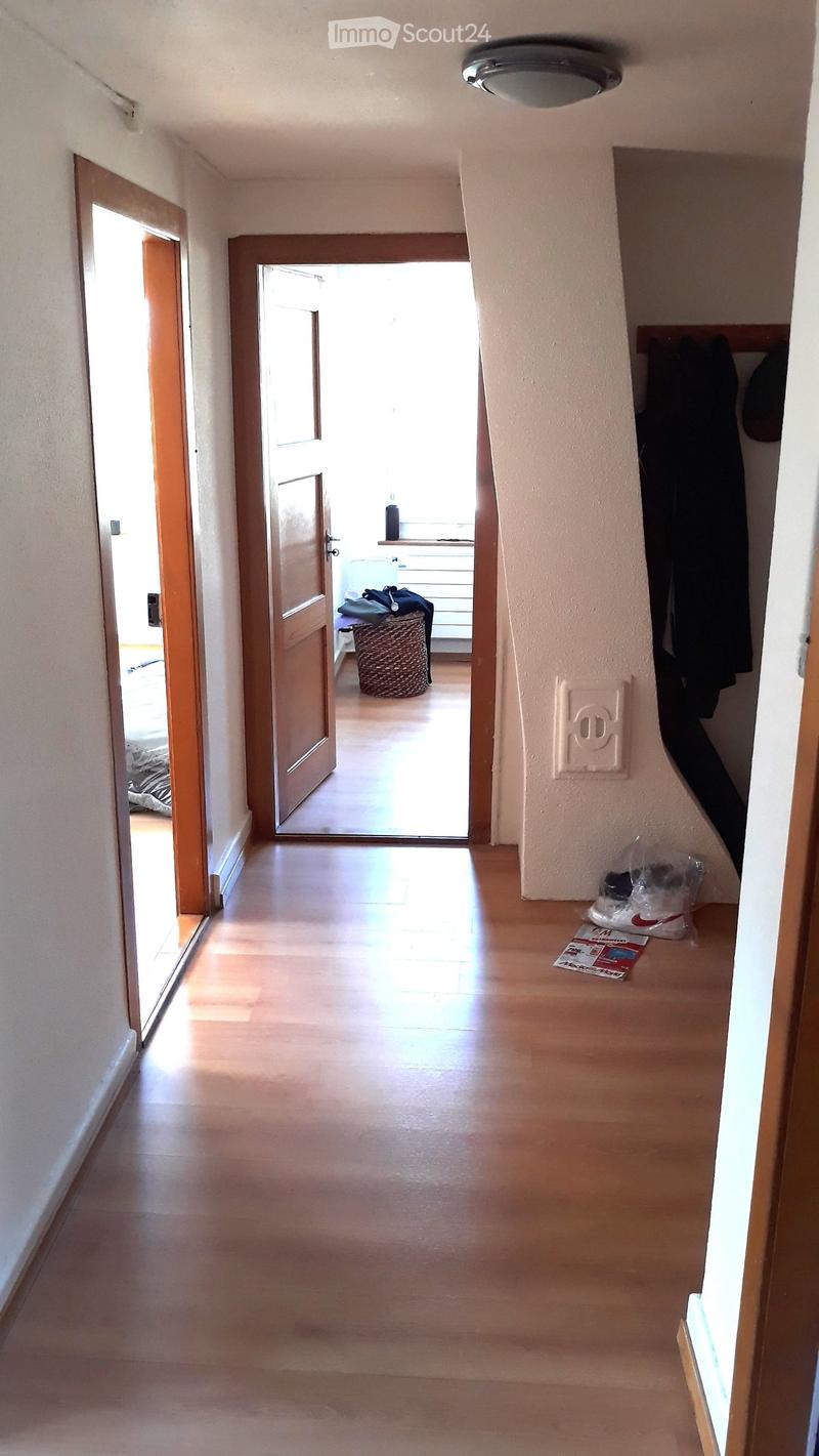 A clean, well-lit hallway with wooden flooring and white walls. Open doors lead to adjacent rooms, and a coat rack is visible on the right side.