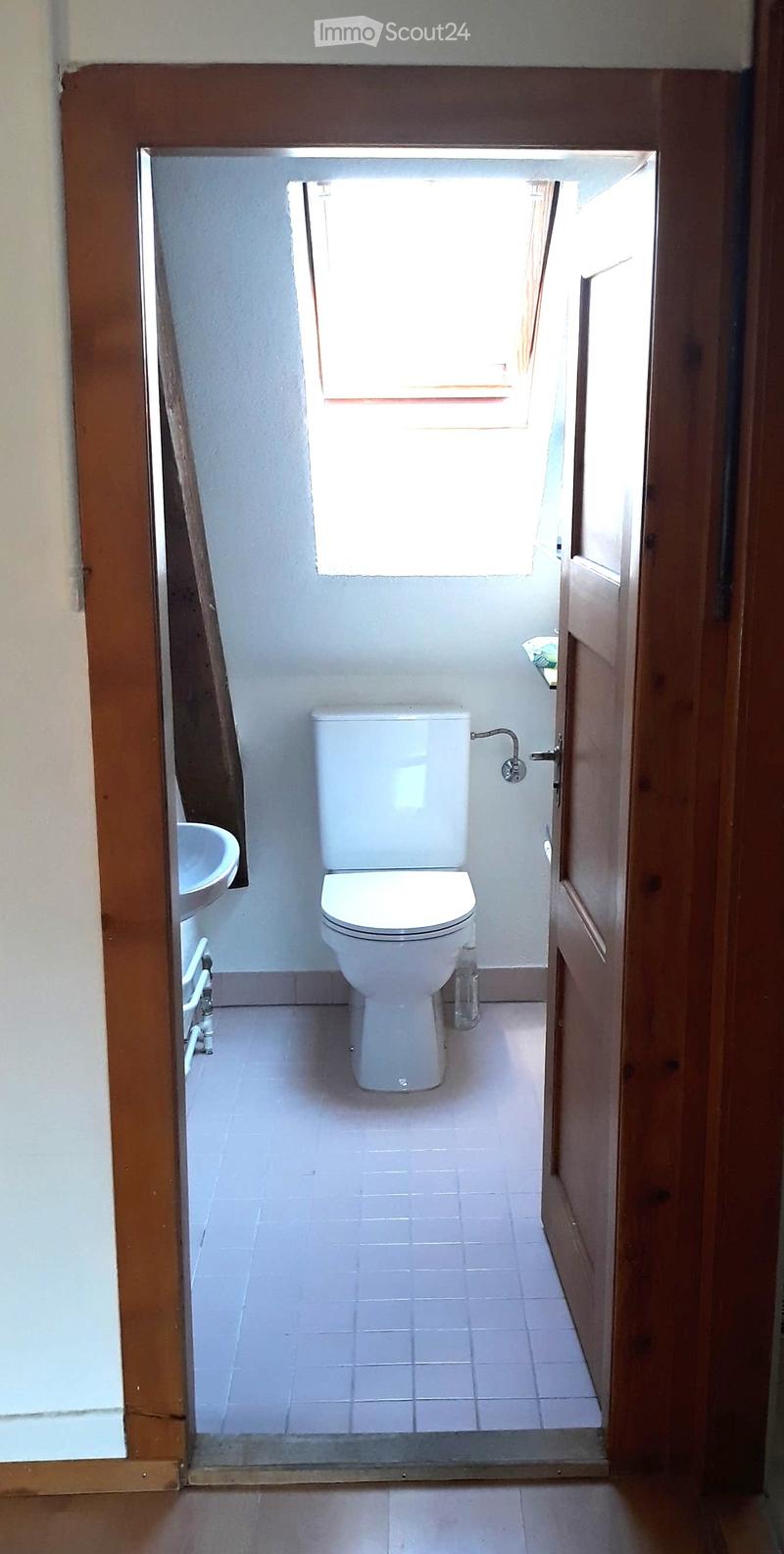 Small bathroom with white tiled floor and walls, toilet, sink, and a window above the toilet.
